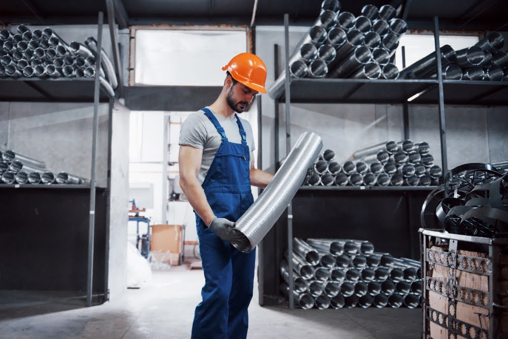 A technician holding a metal tube in a factory storage room.